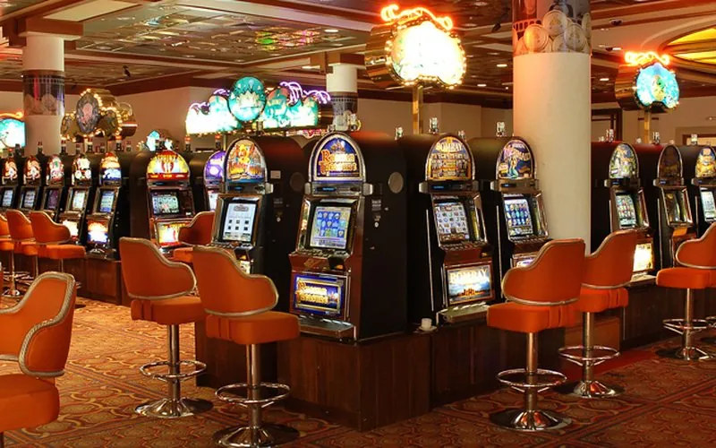 Rows of lit slot machines with orange stools in a casino hall